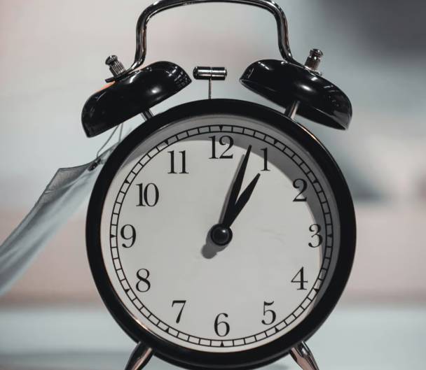 Vintage black alarm clock showing 11:59, closeup on gray background. Concept of time running out or approaching deadline. Retro style timepiece.