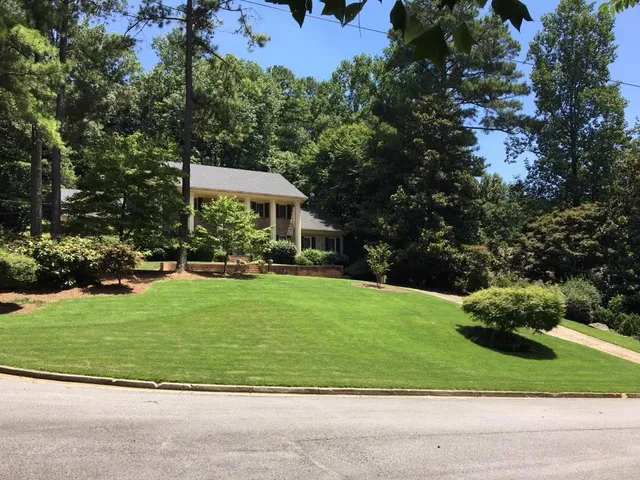 Lush green lawn surrounded by trees leads to an inviting suburban home on a sunny day.