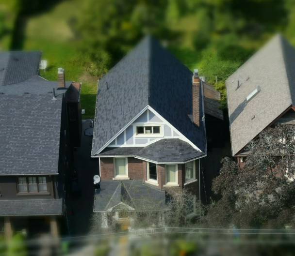 Aerial view of suburban houses with contrasting roof colors and styles, surrounded by lush green trees, creating an idyllic neighborhood setting.